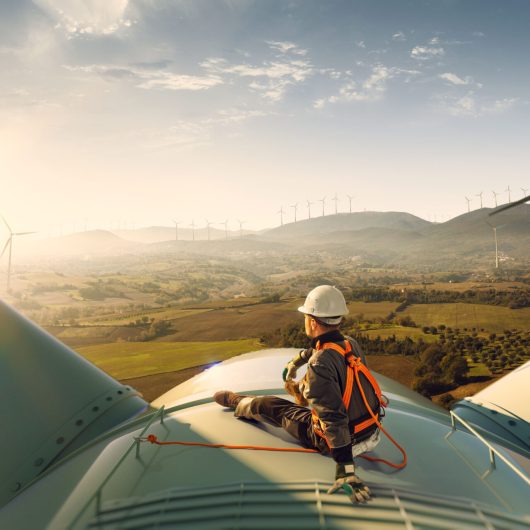 Happy engineer feel success after good work. He standing a top of windmill and looking beautiful sunset landscape